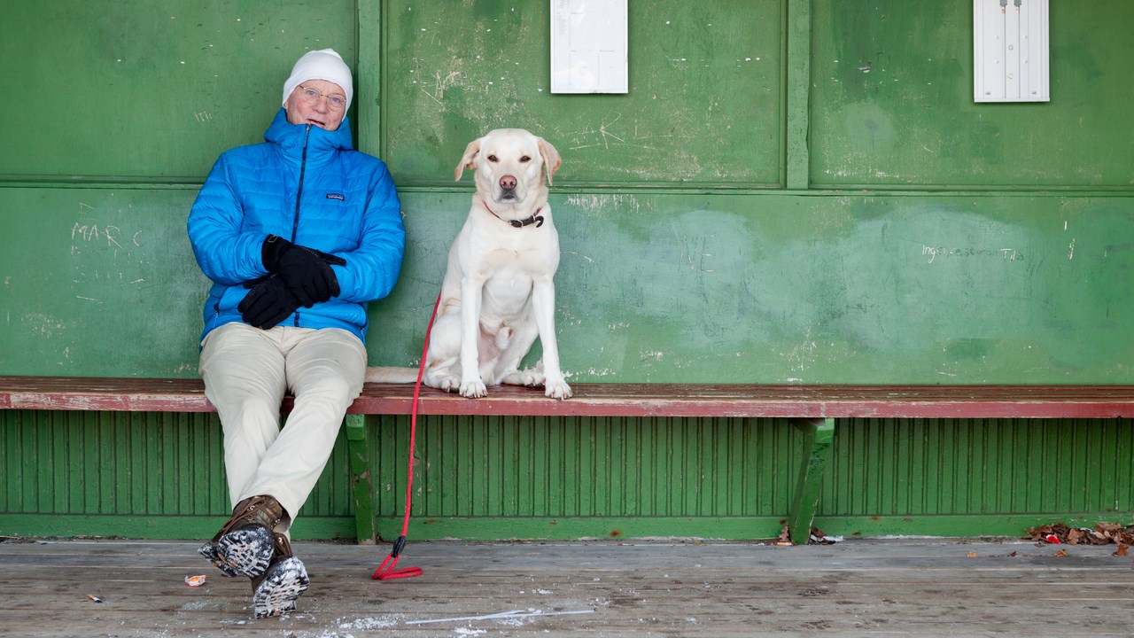 Hundägare i vinterjacka sitter på bänk med stor hund bredvid