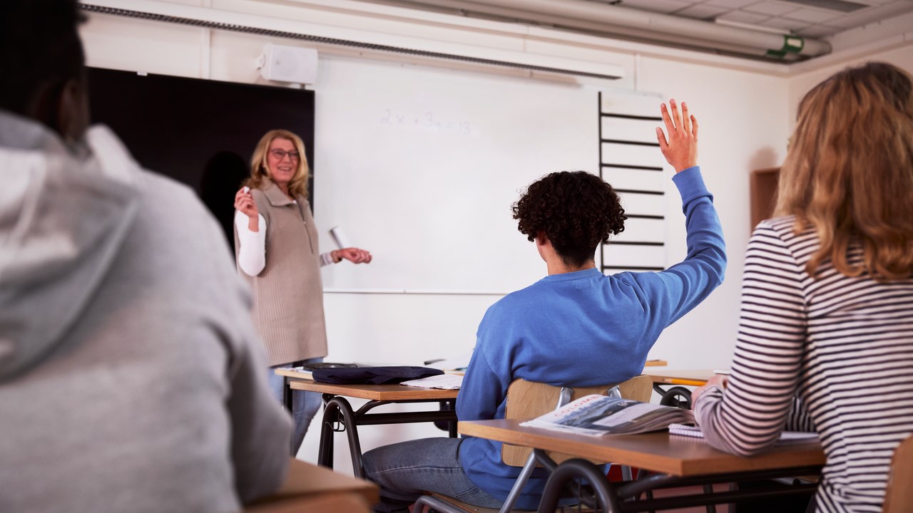 En person räcker upp handen i ett klassrum.