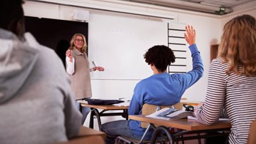 En person räcker upp handen i ett klassrum.