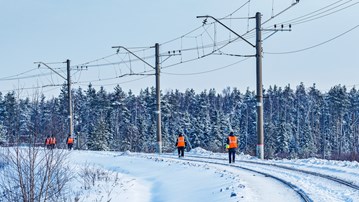 Banarbetare går på räls i vinterlandskap.