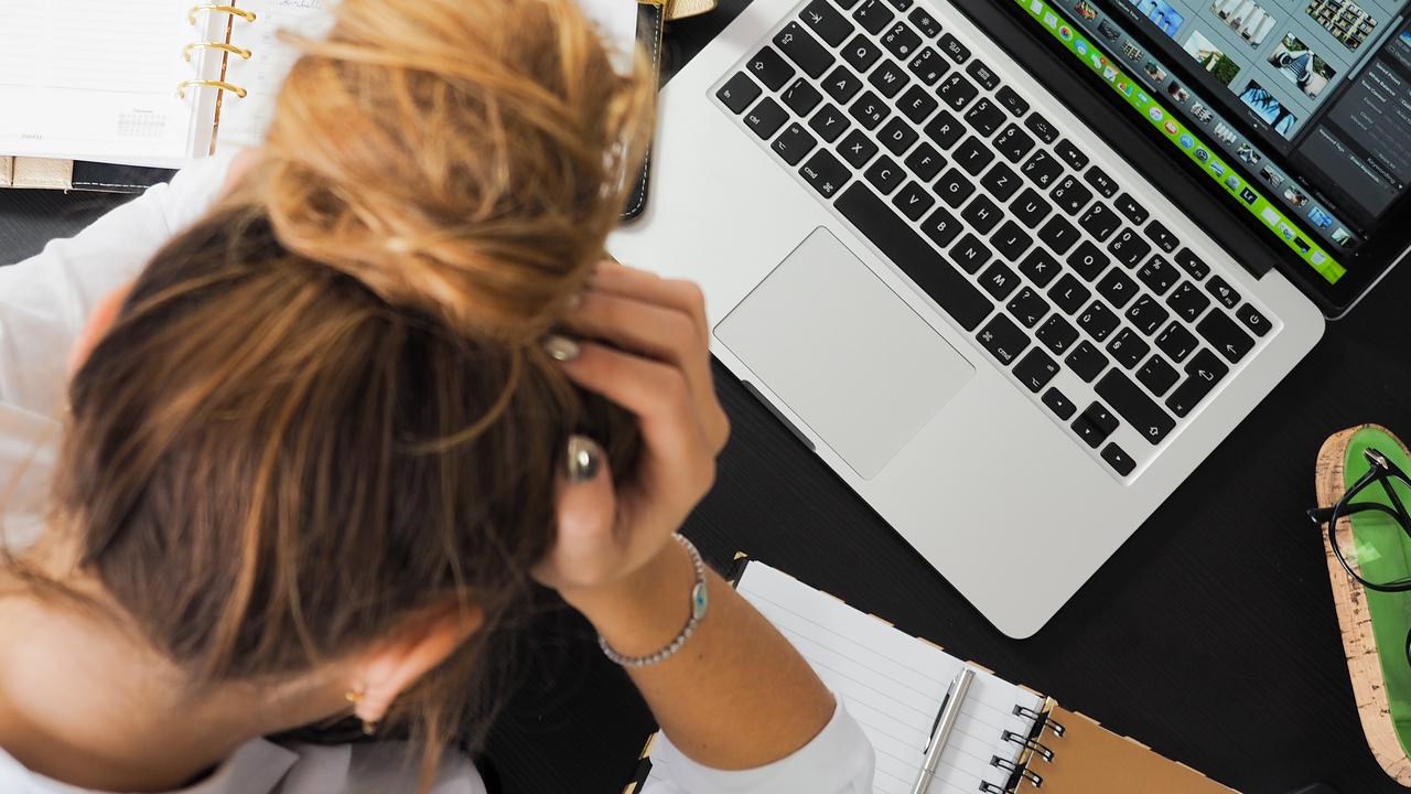 Kvinna sitter med huvudet i händerna vid skrivbord med dator