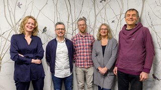Five researchers stand in a room against a wall with forest bird wallpaper