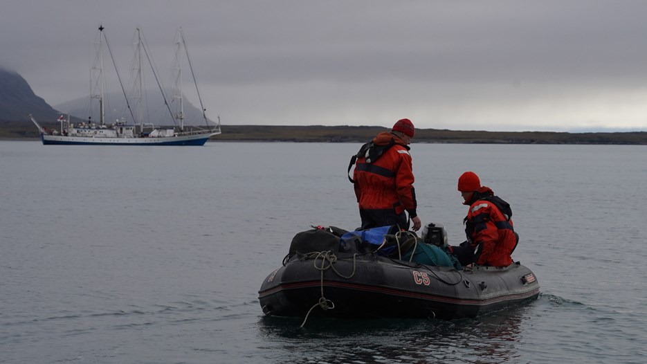 Two people on a small boat, and a bigger boat in the background.