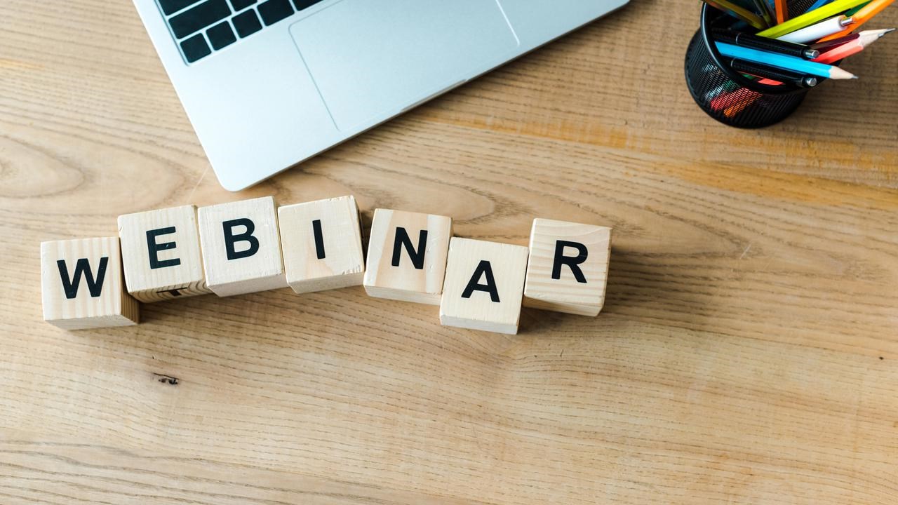 Träklossar på skrivbord bredvid laptop som bildar ordet webinar.
