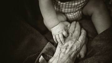 En äldre och en baby hand håller varandra