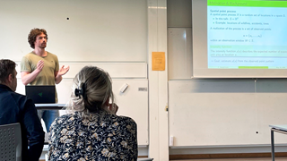 A group of people sitting around a table in front of a projector screen.