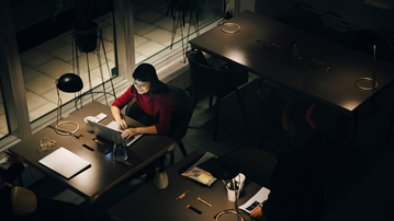 A woman sat working at a laptop in a dimly lit open plan office.
