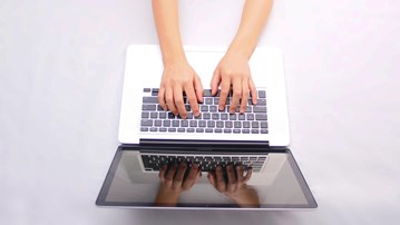 En person skriver på en laptop.