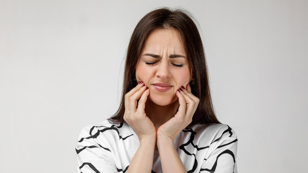 Kvinna med tandv&auml;rk som h&aring;ller om k&auml;karna och grimaserar.