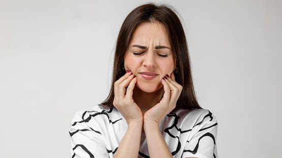 Kvinna med tandvärk som håller om käkarna och grimaserar.