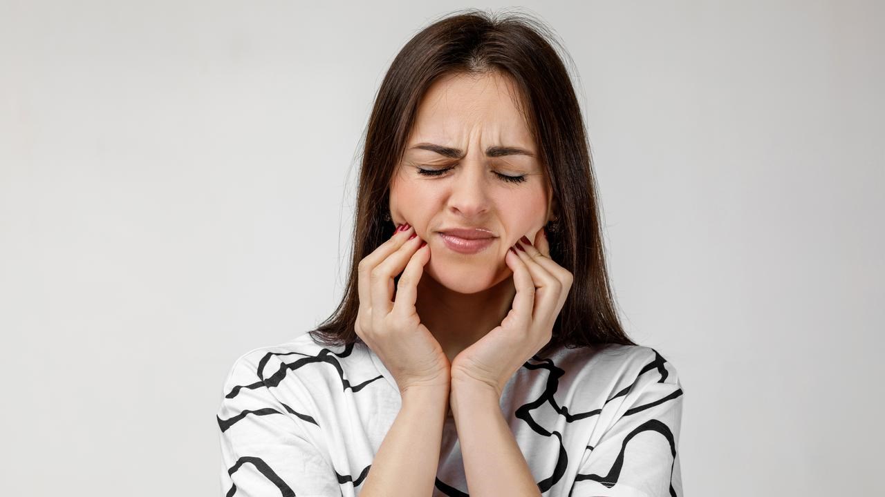 Kvinna med tandvärk som håller om käkarna och grimaserar.