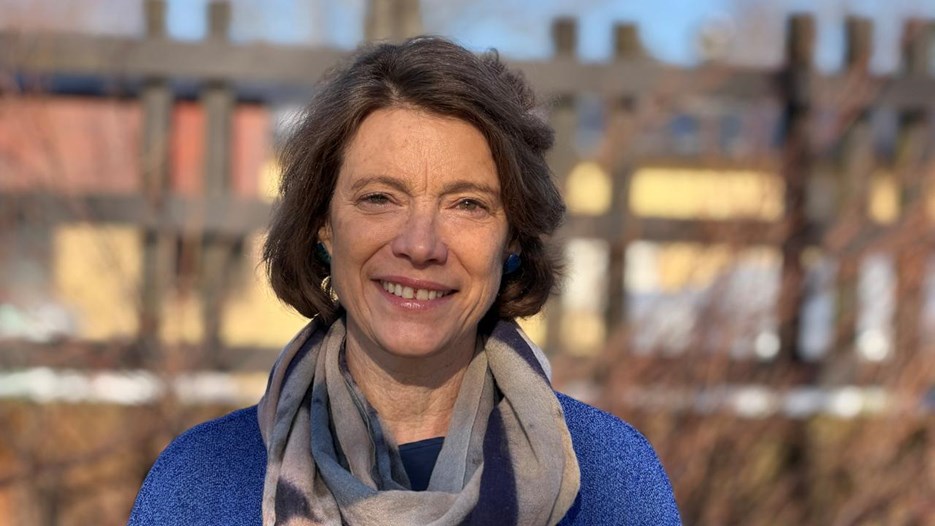 Karen O'brien står utomhus och ler i en blå tröja och scarf.