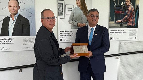 Two men in suits poses with a gift: a plaque with wooden frames.