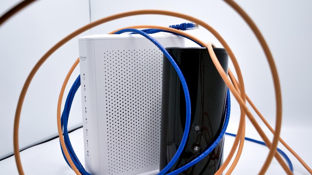 Svart och vit router omgiven av blå och orange internetkablar.