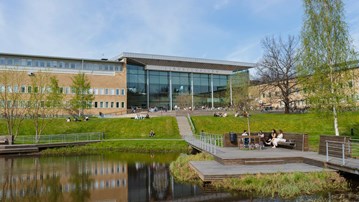 Bild på campusdammen och studenter sittande på brygga