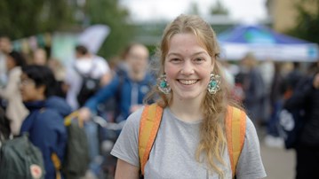Ung kvinna med ryggsäck framför en större mängd människor