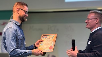 En man mottar ett diplom av en man som håller i en mikrofon.