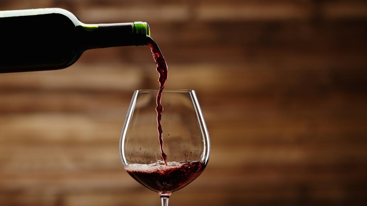 Häller rödvin ur en vinflaska i ett vinglas mot en bakgrund av trä.