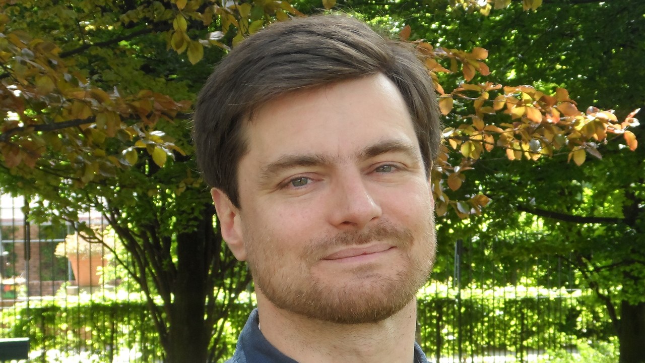 Porträttbild föreställande Nicolas Sabouret i blå skjorta med gröna träd i bakgrunden.