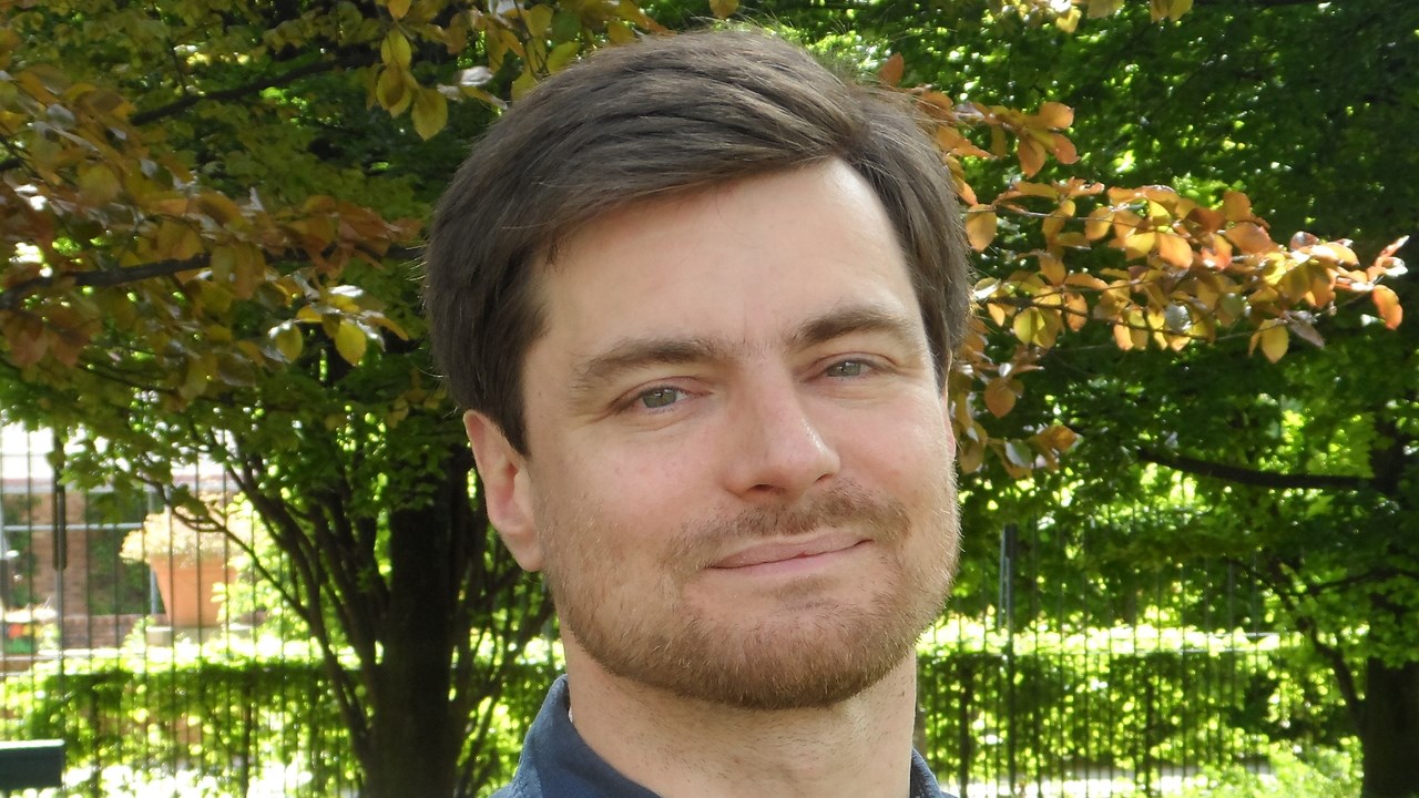 Porträttbild föreställande Nicolas Sabouret i blå skjorta med gröna träd i bakgrunden.