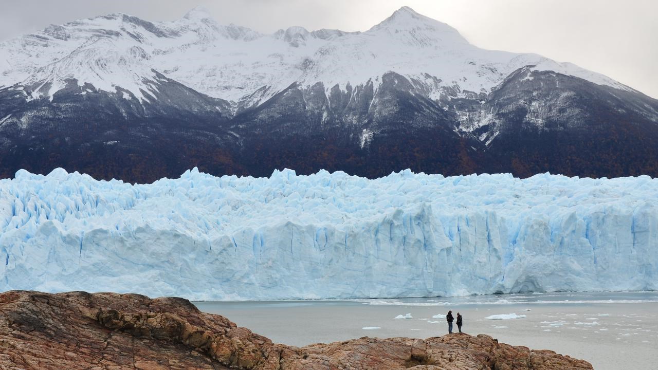 Människor i fjärran med glaciärer och berg i bakgrunden.