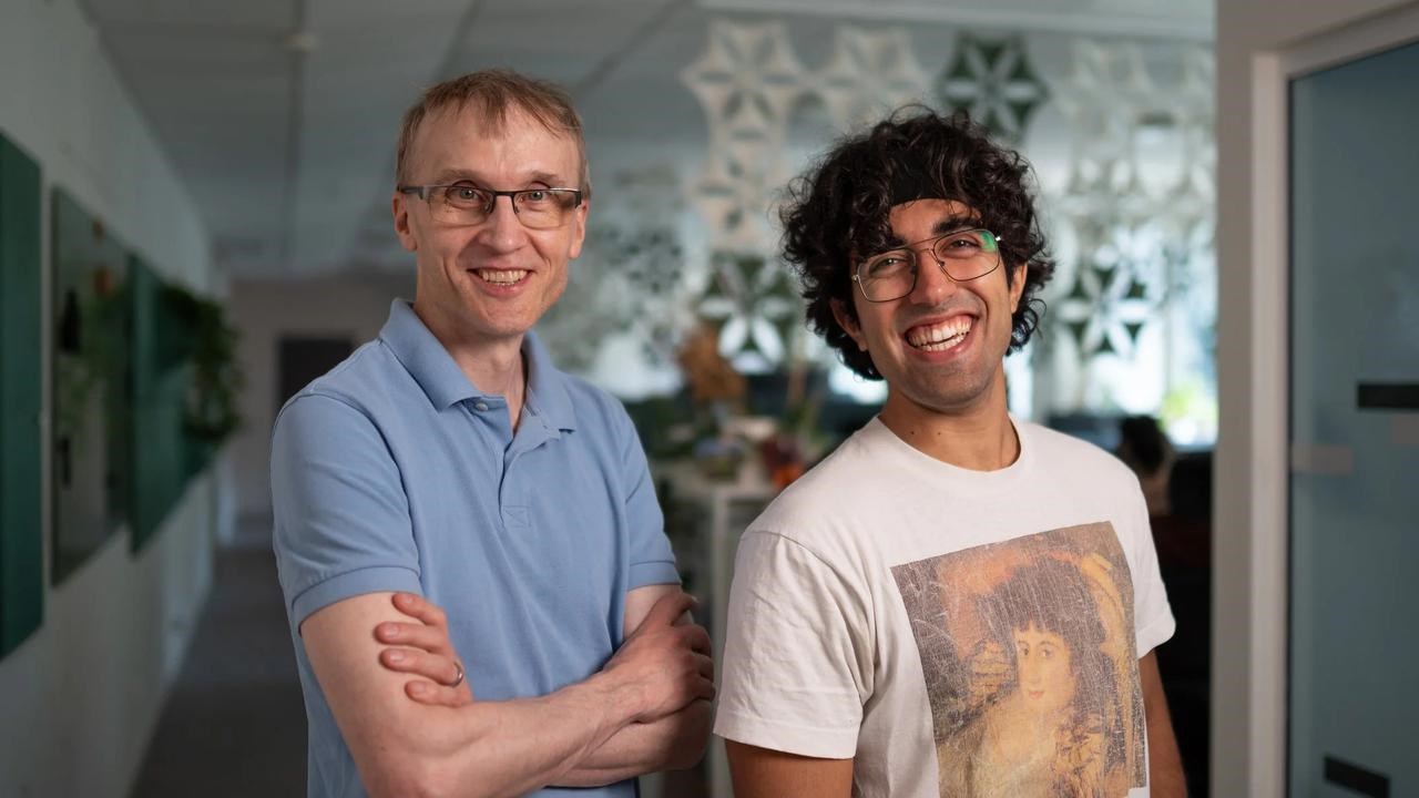 Portrait of two men in an open plan office.