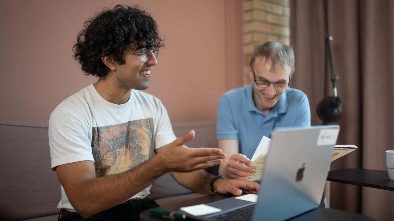 Two men in discussion around a laptop at a table.
