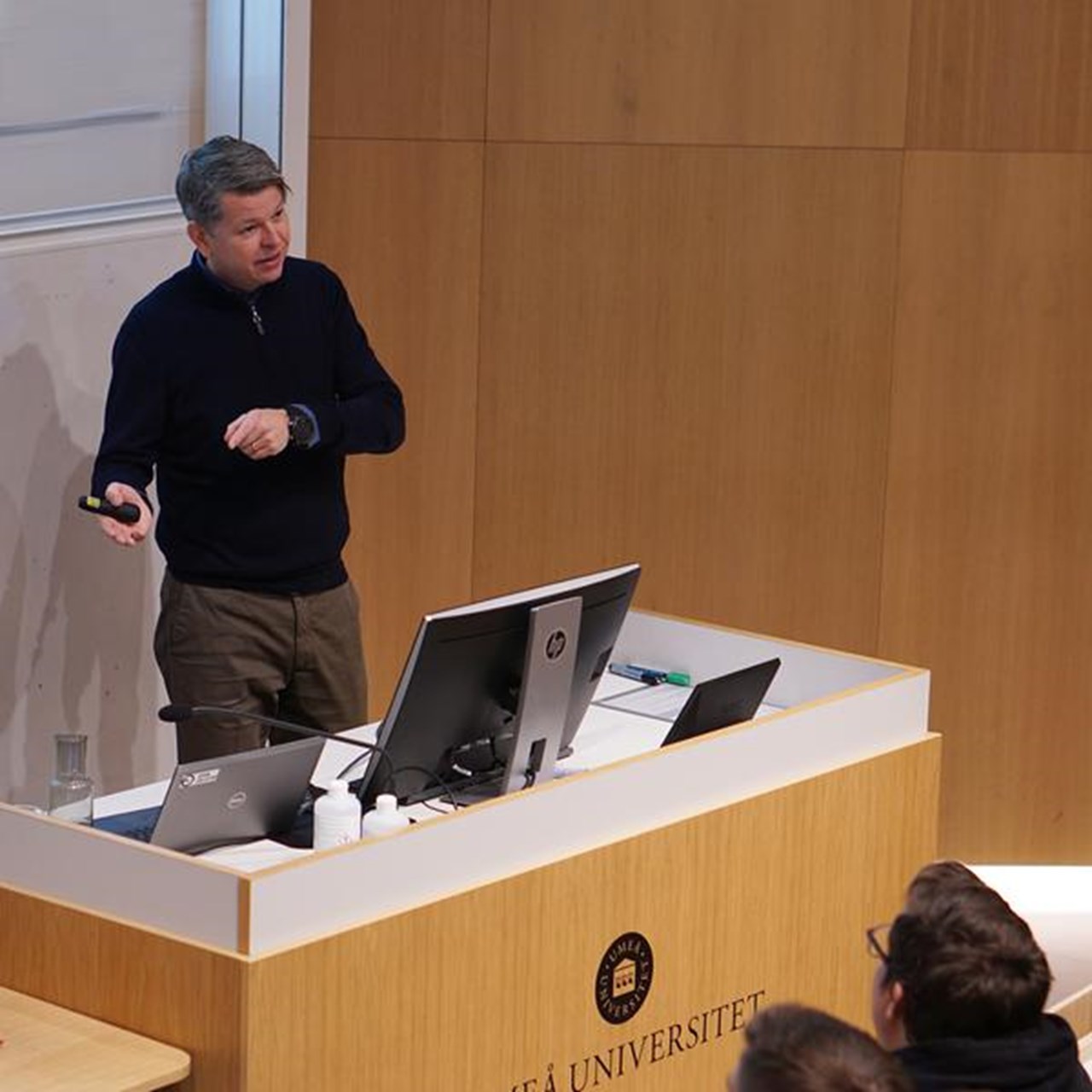 En man som st&aring;r p&aring; ett podium framf&ouml;r en grupp m&auml;nniskor.