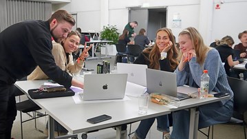 En man och tre kvinnor som arbetar tillsammans vid ett bort. På bordetsyns datorer.