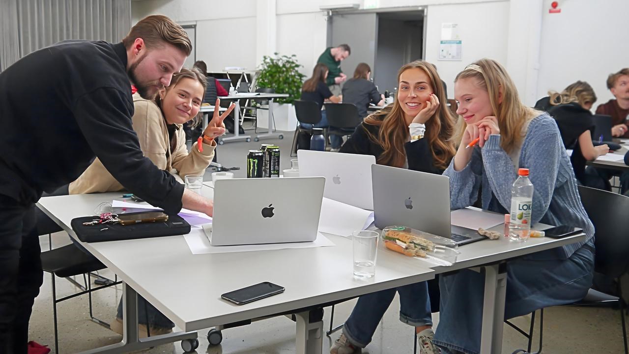 En man och tre kvinnor som arbetar tillsammans vid ett bort. P&aring; bordetsyns datorer.