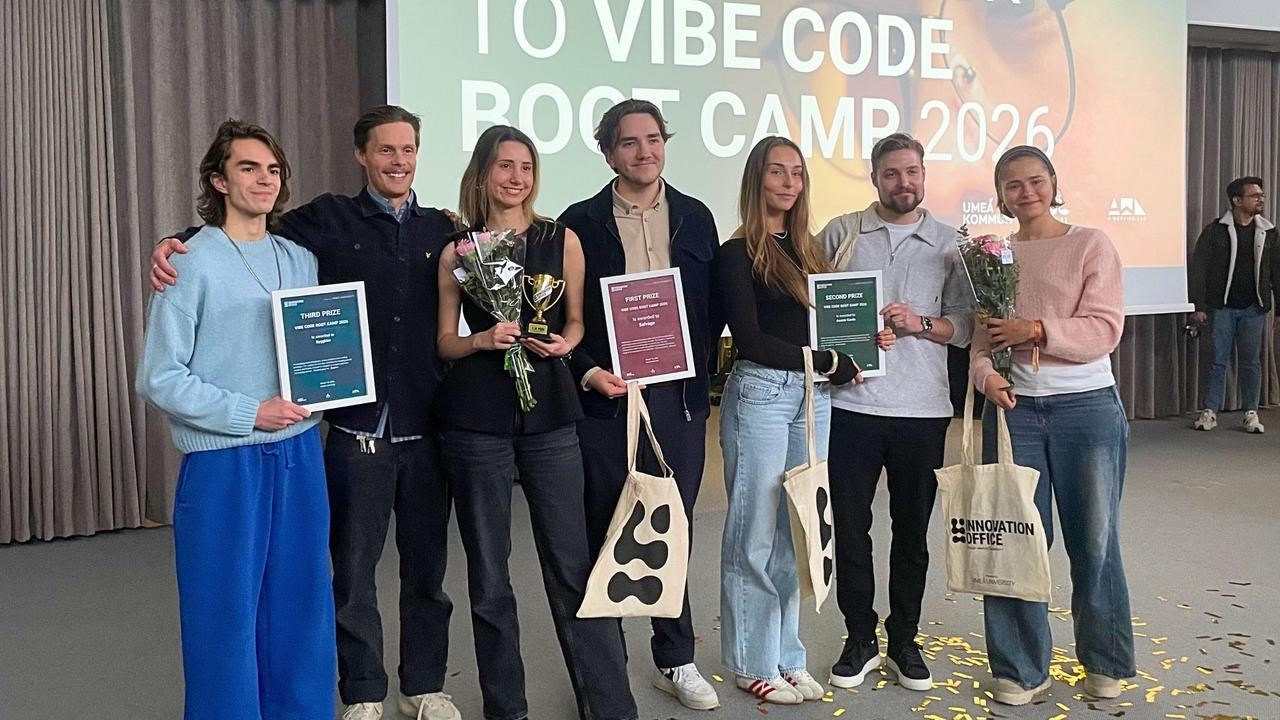 Bilden f&ouml;rest&auml;ller sju personer som h&aring;ller i blommor, tygkassar och diplom. I bakgrunden syns texten welcome back to Vibe code Boot Camp 2026 p&aring; sk&auml;rm.