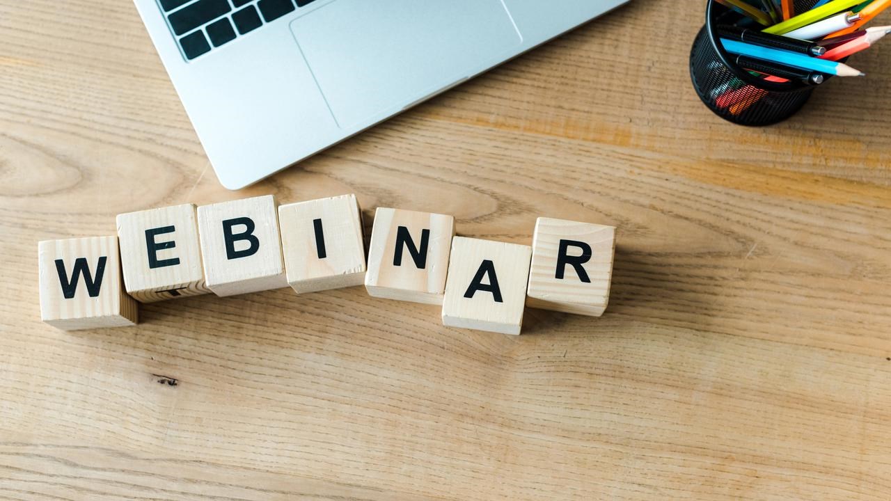 Träklossar på skrivbord bredvid laptop som bildar ordet webinar.