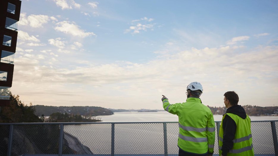 Två män i varselväst pekar mot byggnad