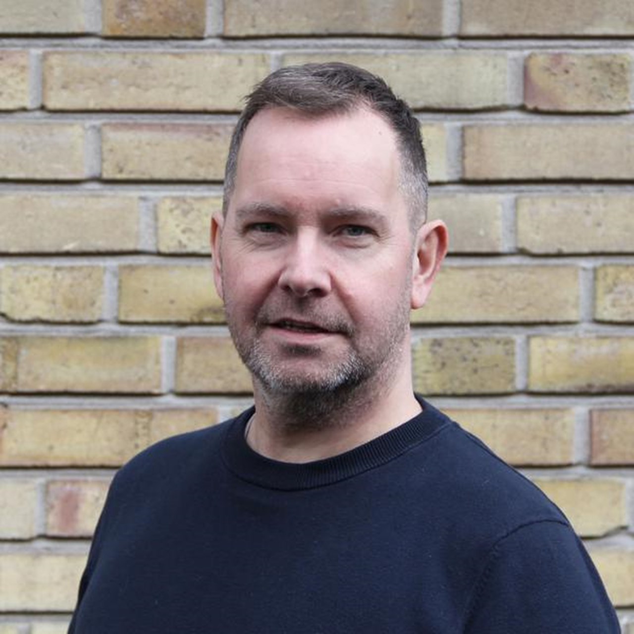 Portr&auml;tt av man framf&ouml;r tegelv&auml;gg