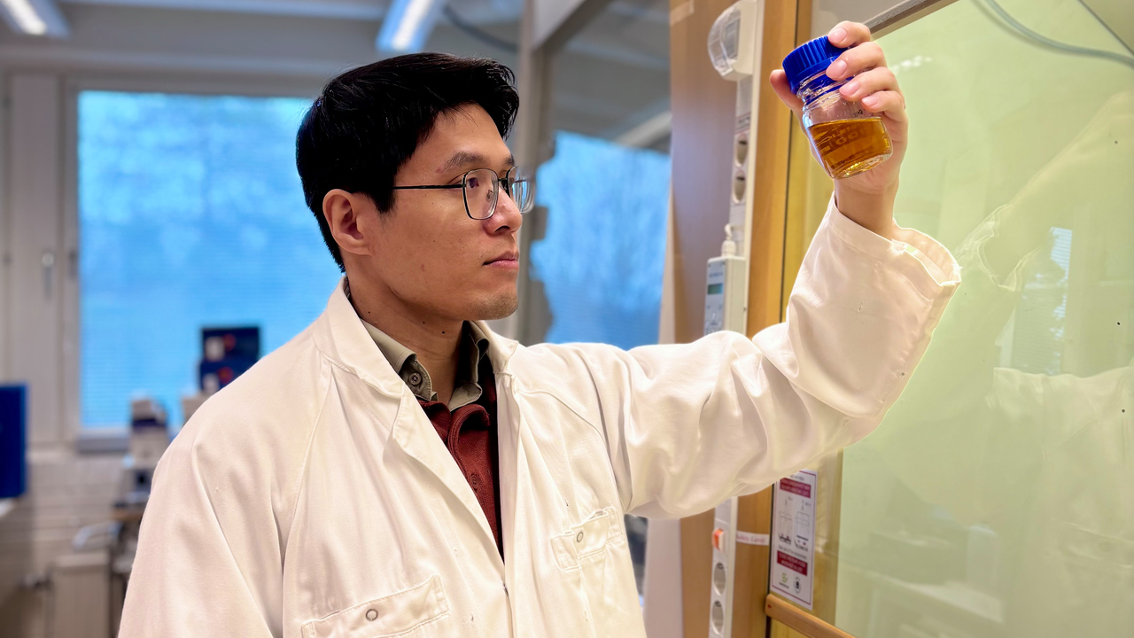 Bild på doktoranden Van Minh Dinh i vit labbrock stående intill ett dragskåp, håller ett preparat i vänstra handen.