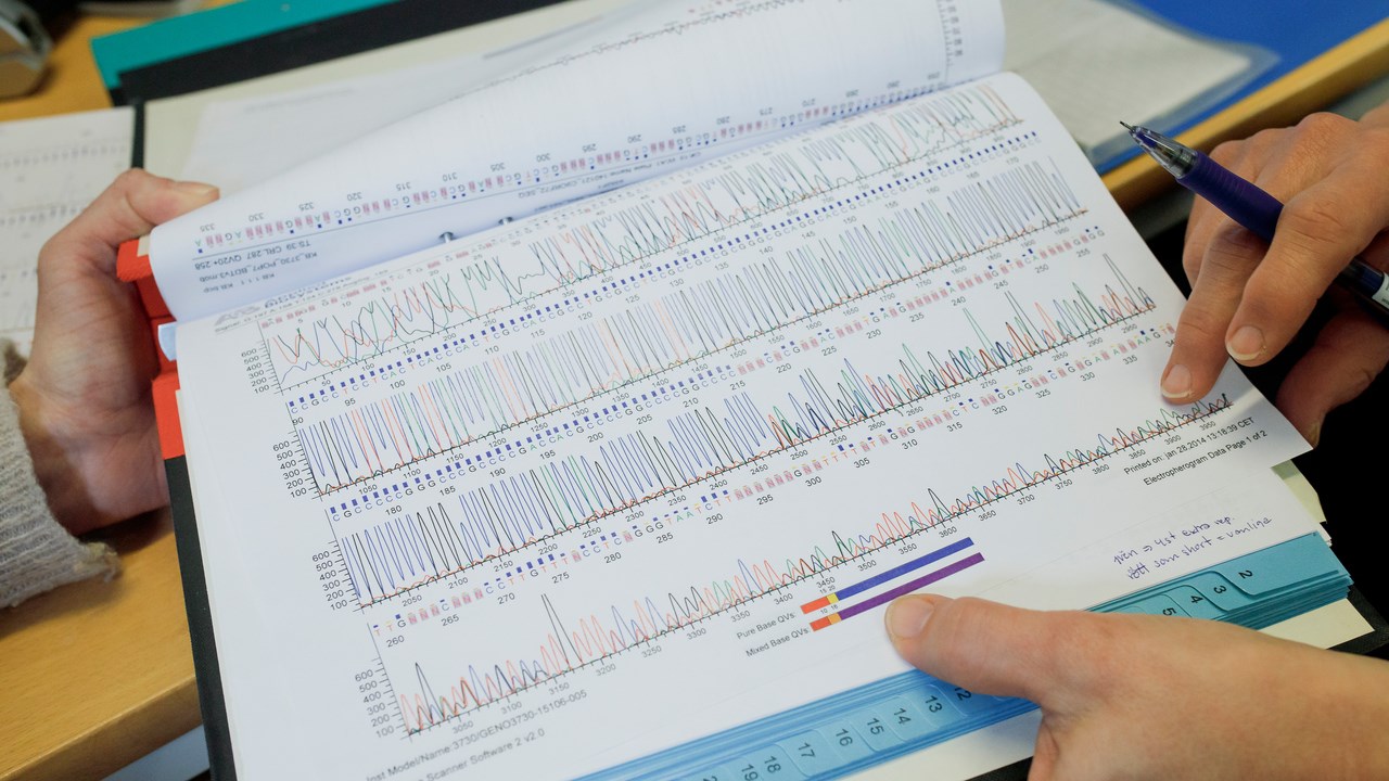 Close-up of an open binder containing sequencing data, and hands holding it.