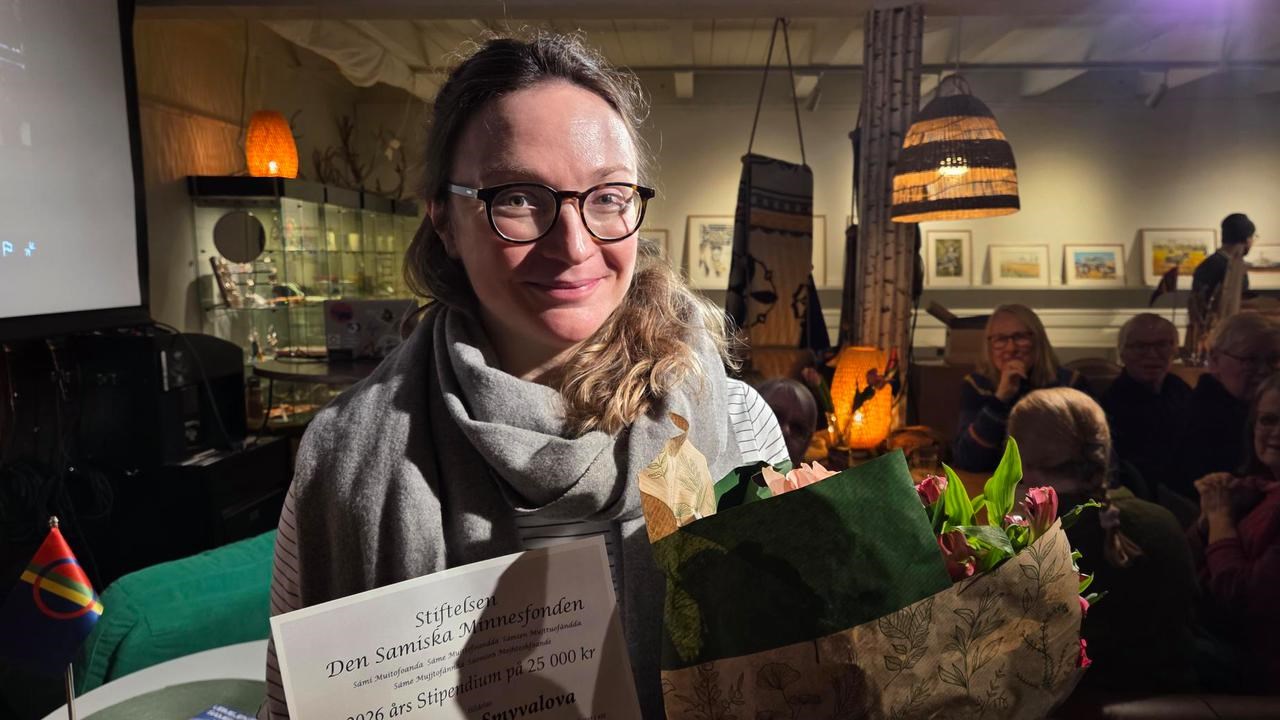 En kvinna som h&aring;ller i en blombukett i ett rum fullt av m&auml;nniskor.