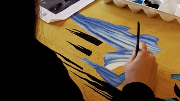 En person målar en tavla på ett bord.