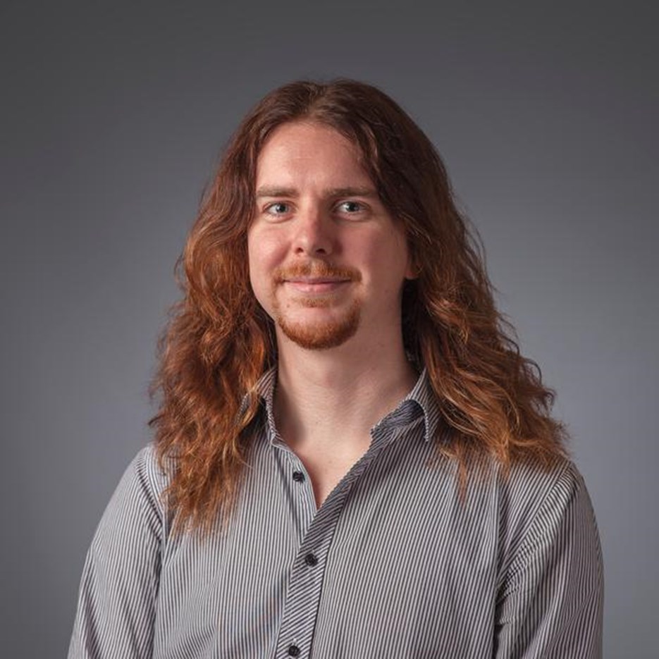 Porträtt på Jakob Wickzell. Han har axellångt brunt hår och en grå skjorta.