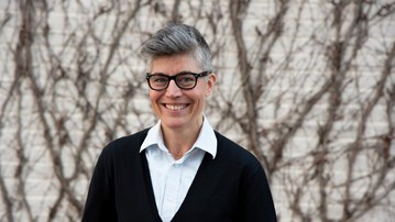 Forskaren Matilda Wurm står framför en tegelvägg med slingrande växtlighet. Hen ler mot kameran.