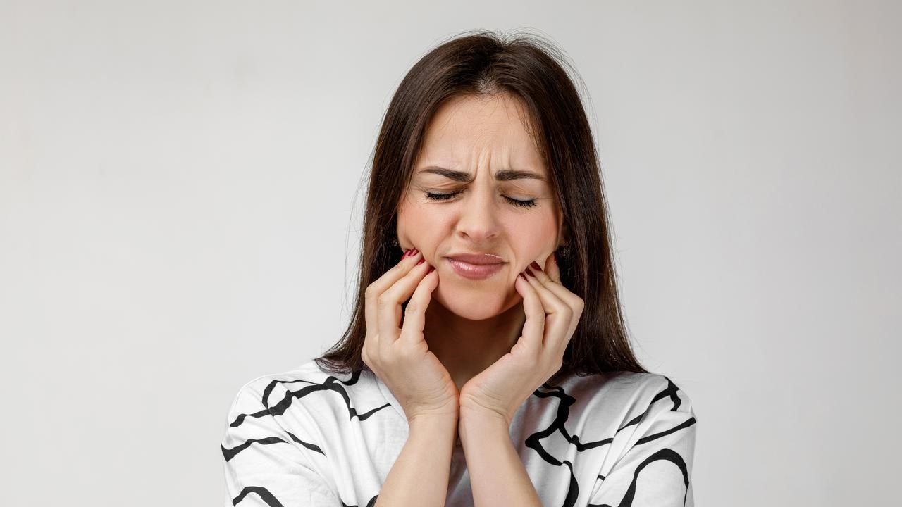 Kvinna med tandvärk som håller om käkarna och grimaserar.