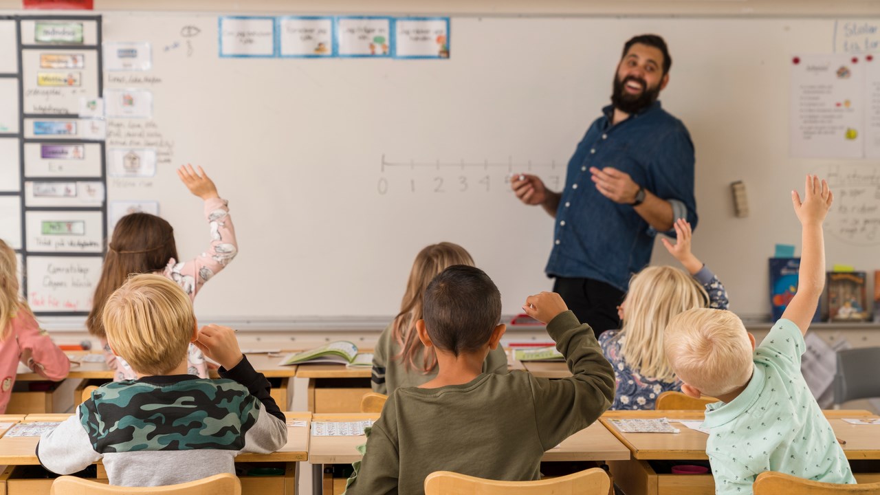 Barn i klassrum räcker upp handen.