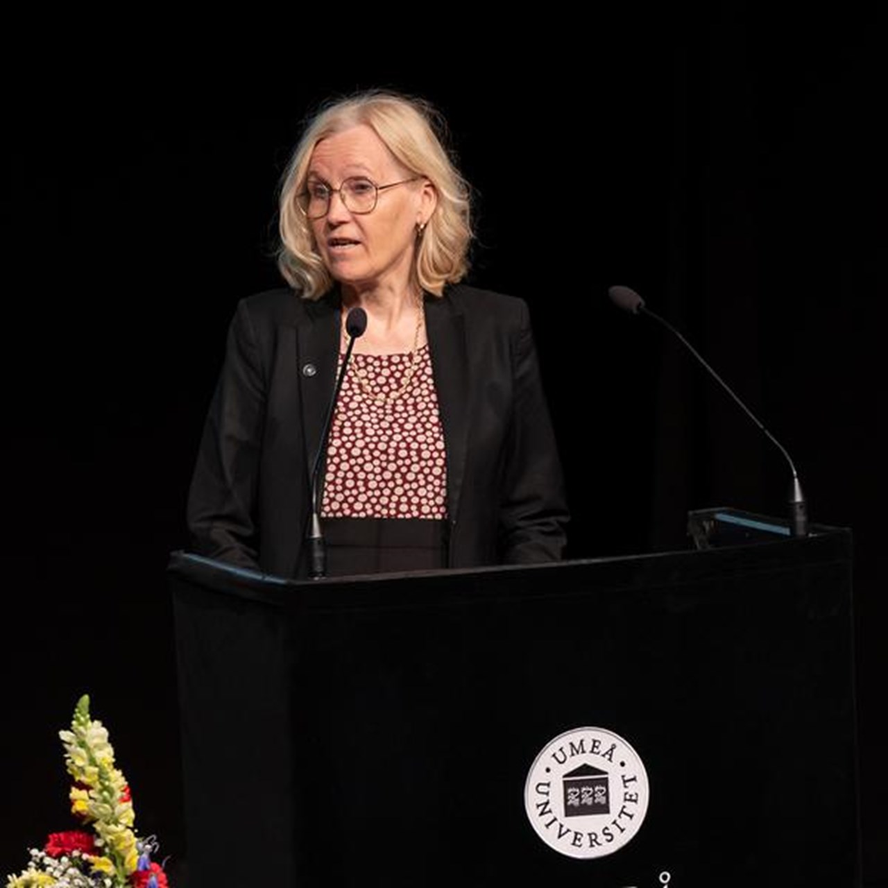 En kvinna st&aring;r p&aring; ett podium framf&ouml;r en mikrofon.