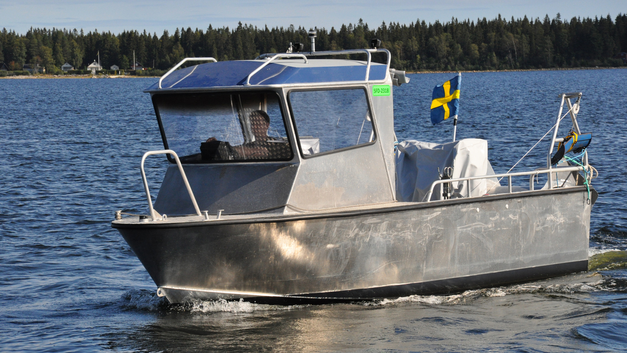 En b&aring;t av metall med stor hytt i f&ouml;ren och flagga i aktern