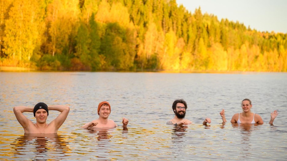 Four people swim in a cold river with autumnal trees behind them