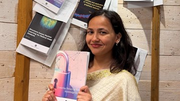 Divya Baura, i mörkt hår och fin klädsel, håller upp sin avhandling under spikningsceremonin.
