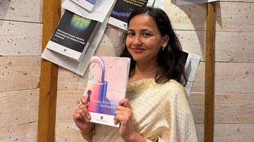 Divya Baura, i mörkt hår och fin klädsel, håller upp sin avhandling under spikningsceremonin.