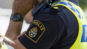 Detalj polis med uniform som pratar i mobil. Man ser arm och tröja med polisens emblem.