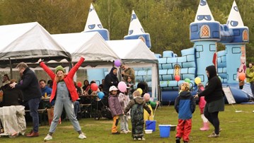 A group of people standing on top of a lush green field in front of tents and a bouncing castle.