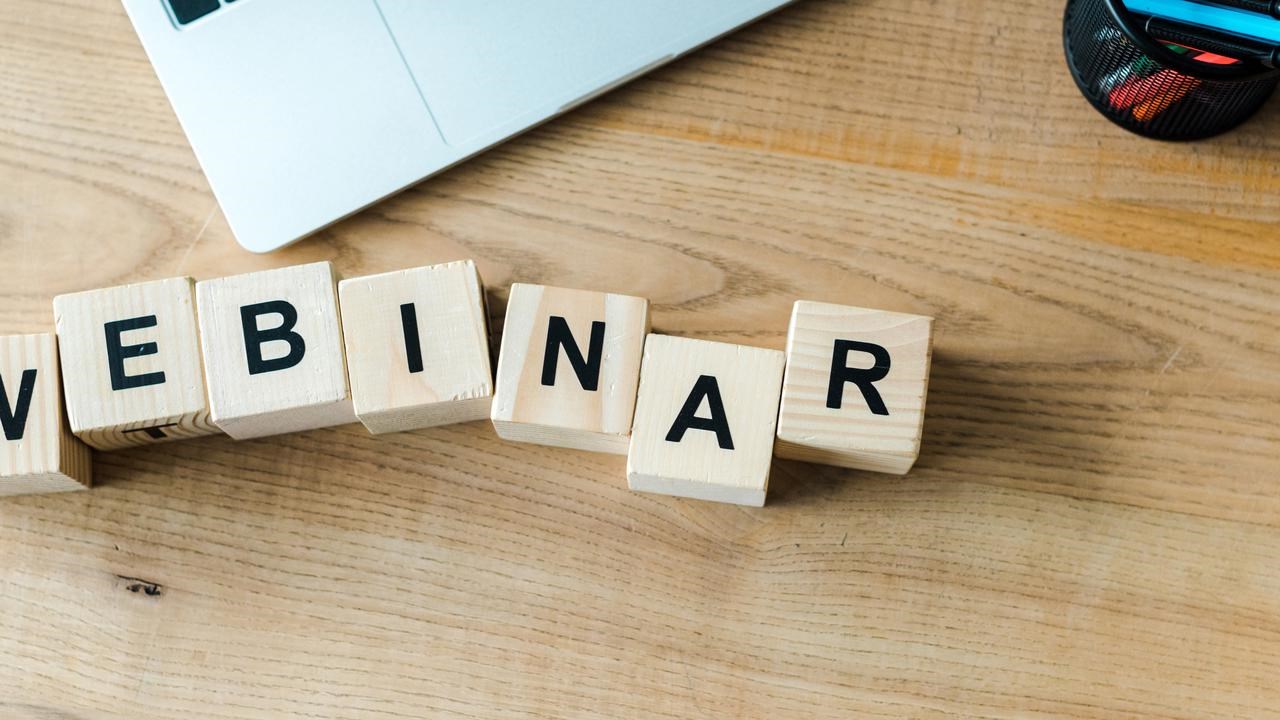 Träklossar på skrivbord bredvid laptop som bildar ordet webinar.